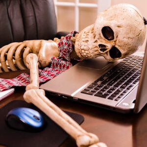 An image of a skeleton sitting in front of a laptop.