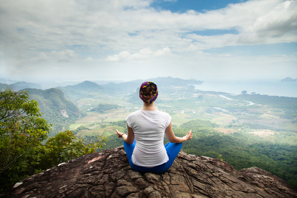 Woman at a mindfulness retreat, meditating on a mountaintop.