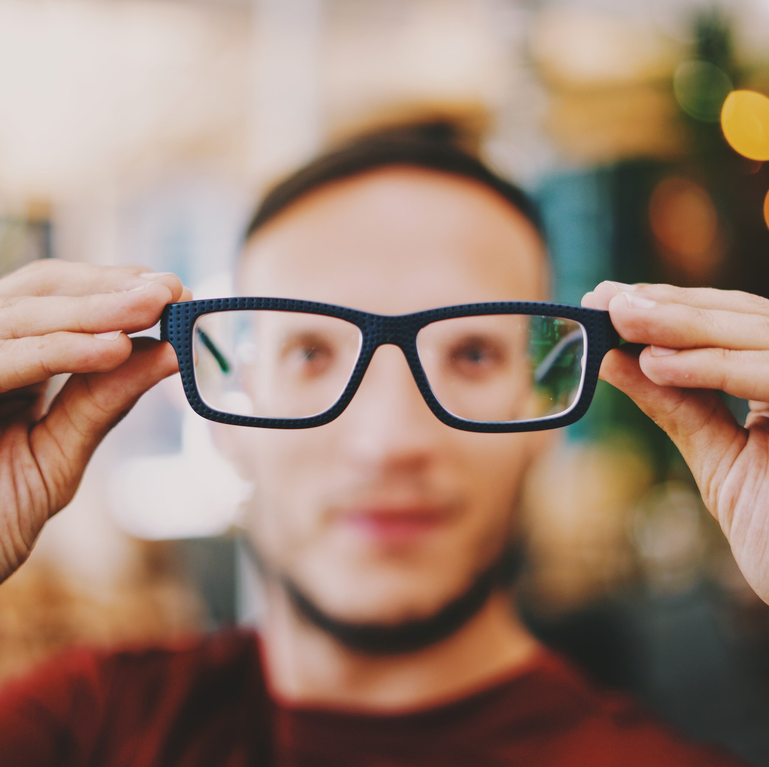 A close up image of an eyeglass and a man with a blurred face who's about to wear it. It shows a poor eye health.