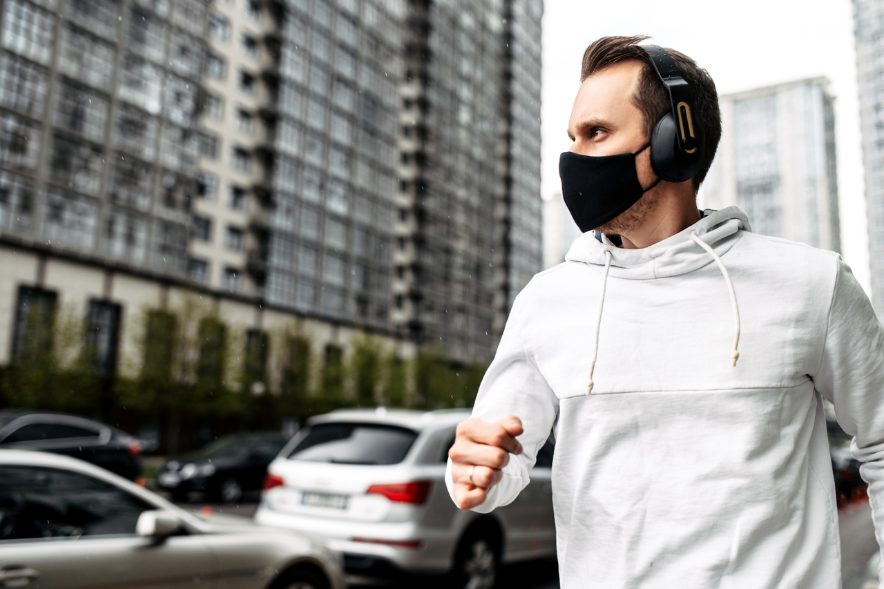 Man is jogging in a protective mask among high-rise buildings.