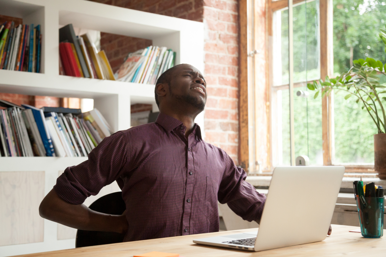 Fatigued casual businessman feeling back pain after sitting on uncomfortable chair for long hours.