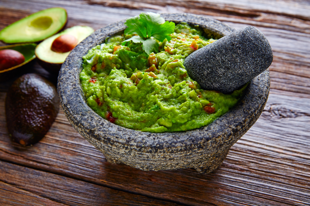 A bowl of guacamole and sliced avocados on the side.