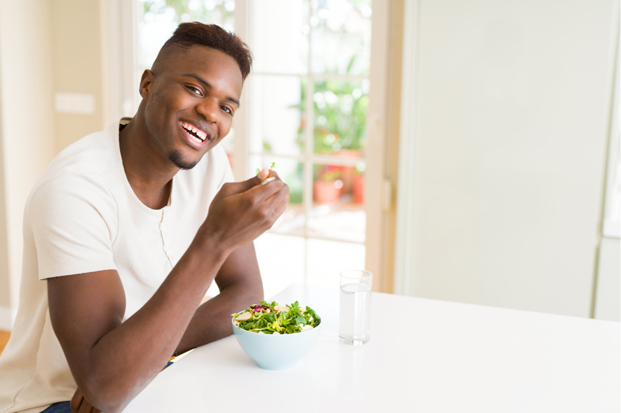 Man eating a healthy vegetable salad using a fork to eat lettuce, happy and smiling sitting on the table