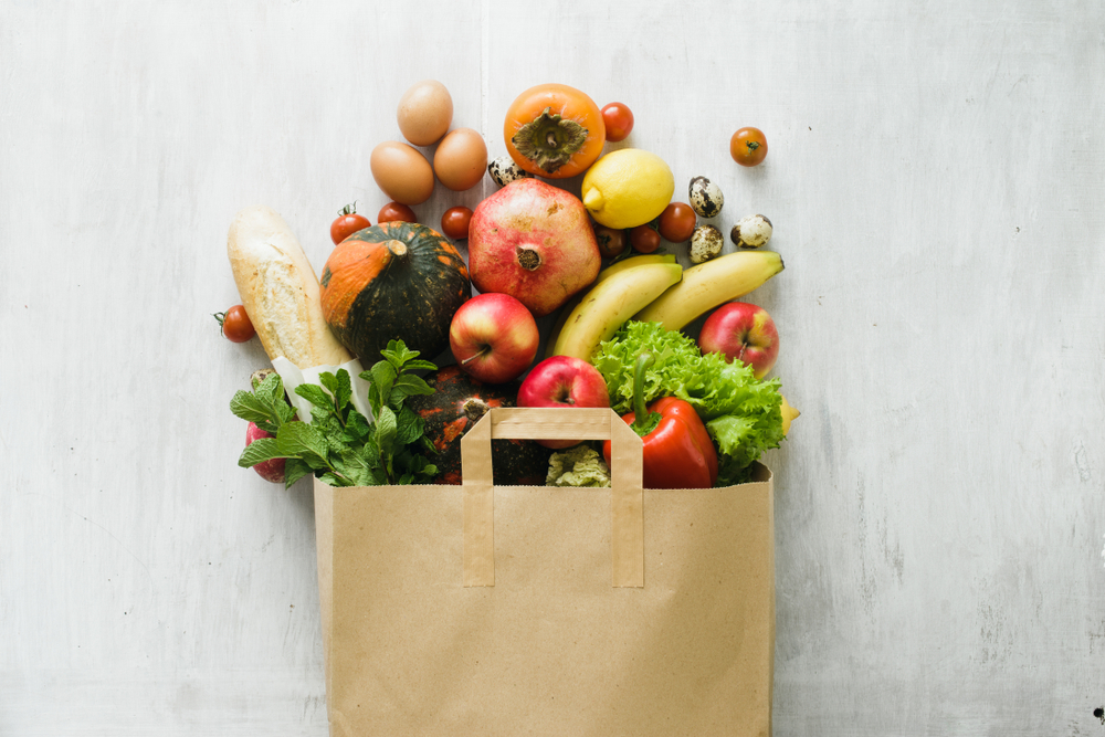 Paper bag of different health food on white wooden background. Top view. Flat lay