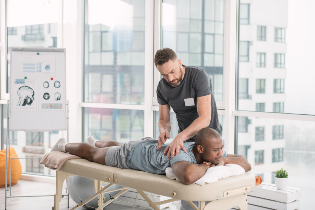 A male therapist doing a back massage to an African American man while explaining the benefits of massage therapy for athletes.