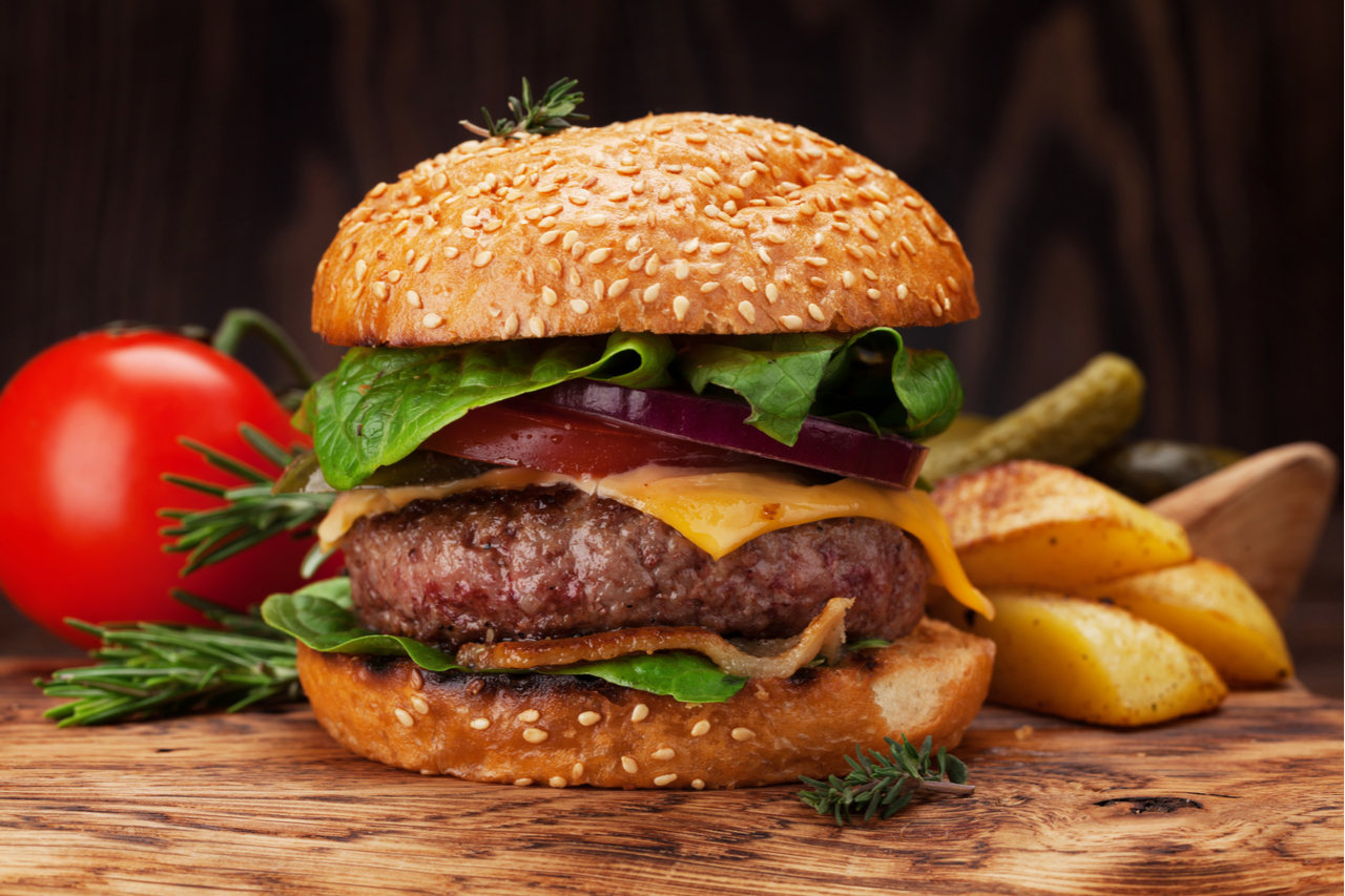 A homemade burger and a fresh tomato and potato fries on the side. 