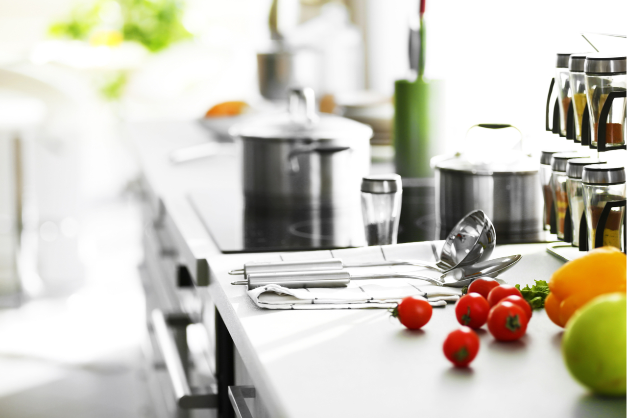 Modern table and electric stove with utensils and vegetables in the kitchen beside window.