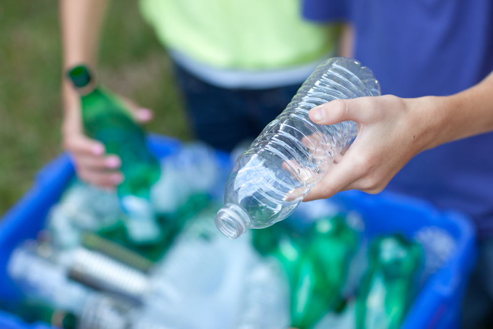 boy and girl putting clear and green bottles and metal cans in recycling blue bin outside in yard