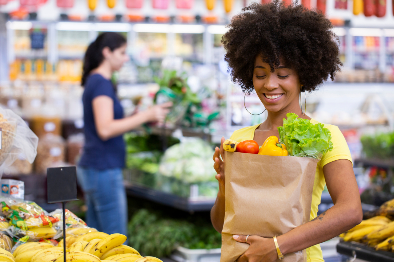 A woman holding a paper bag full of vegetables at the supermarket.