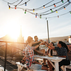 Outdoor shot of young people toasting drinks at a rooftop party. Young friends hanging out with drinks.