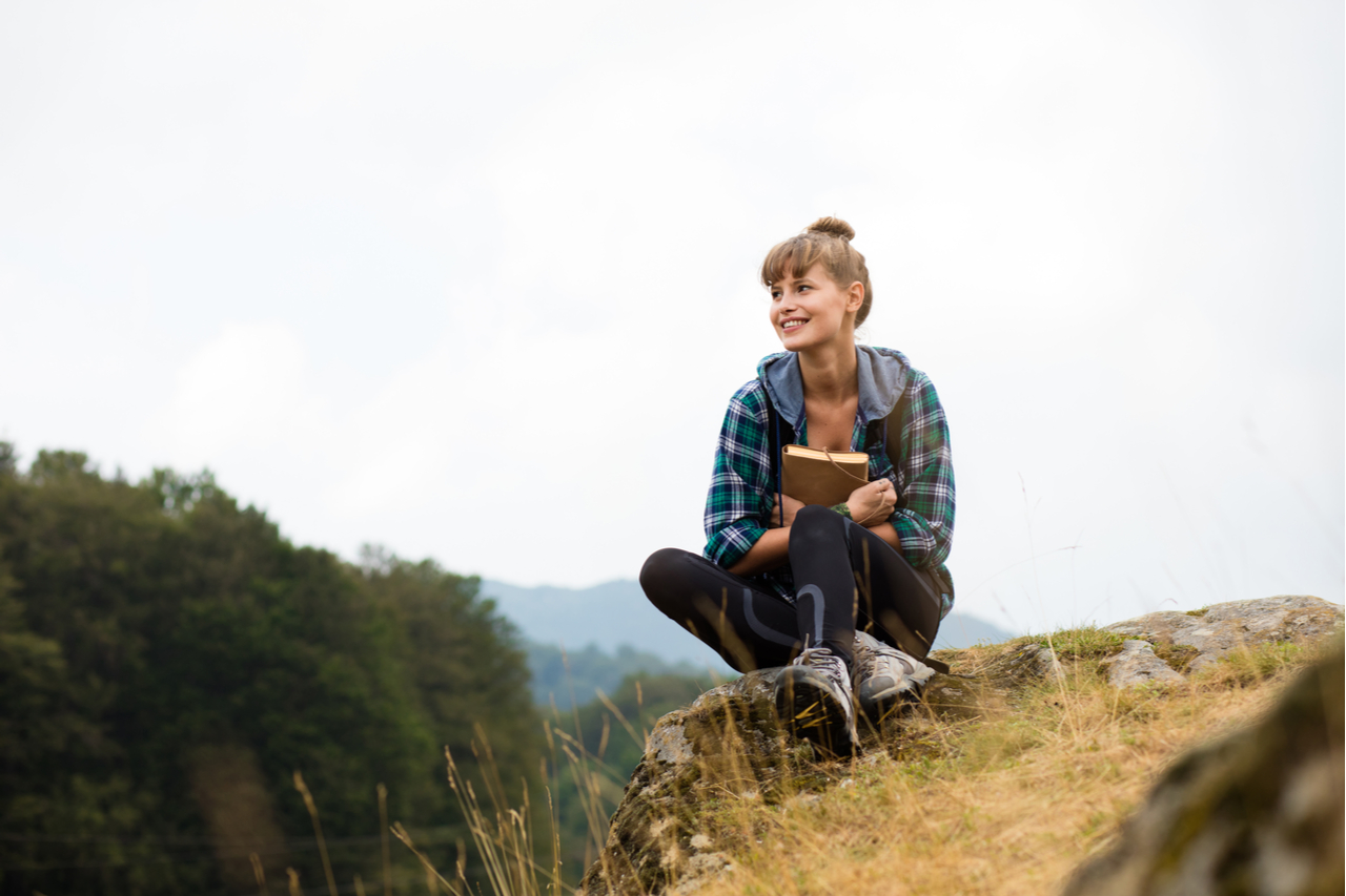 Young sitting on a rock a journal thinking how to get motivated.