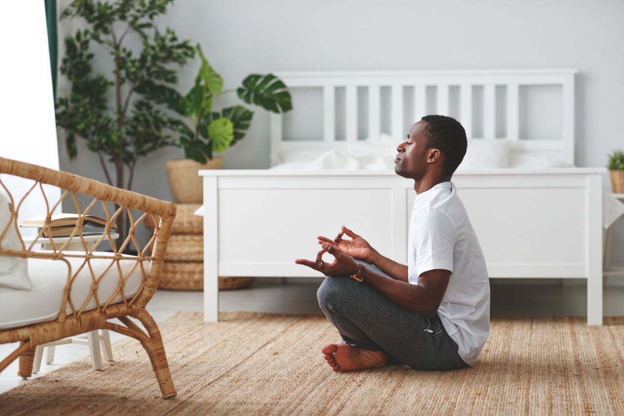 An African American man sitting on a lotus position meditating. 