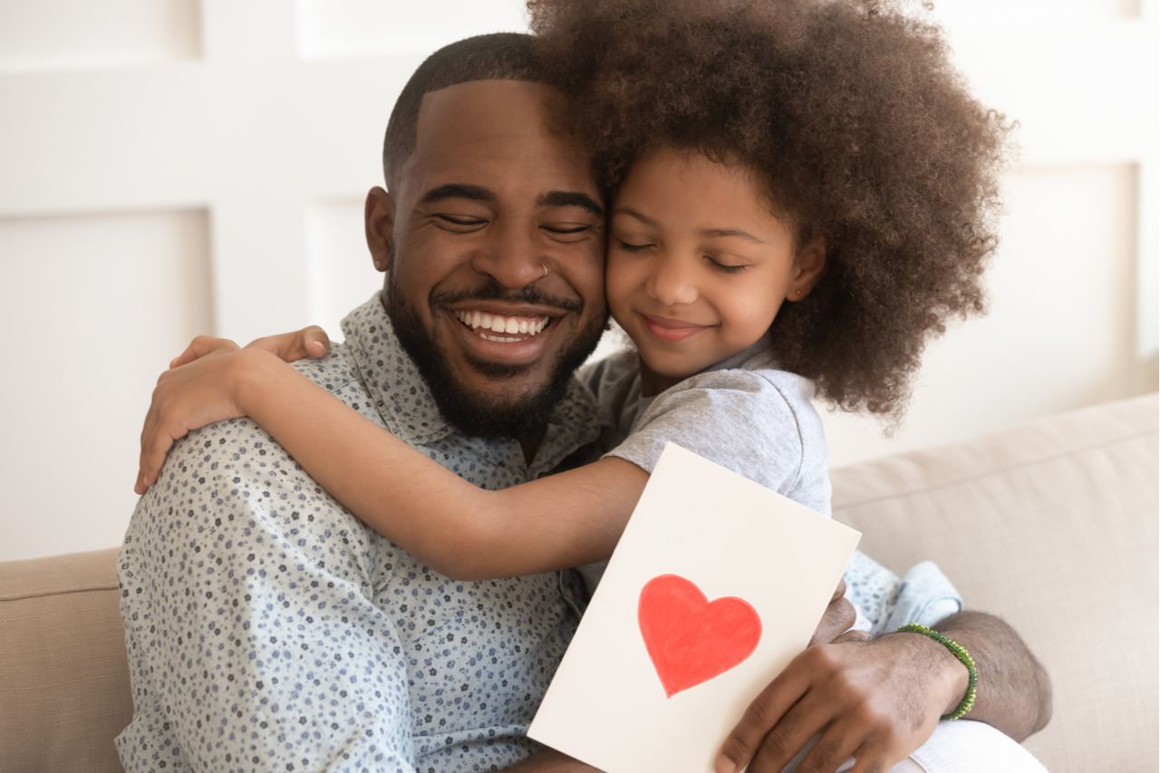 Dad embracing little child daughter holding greeting card with red heart bonding on fathers day concept.