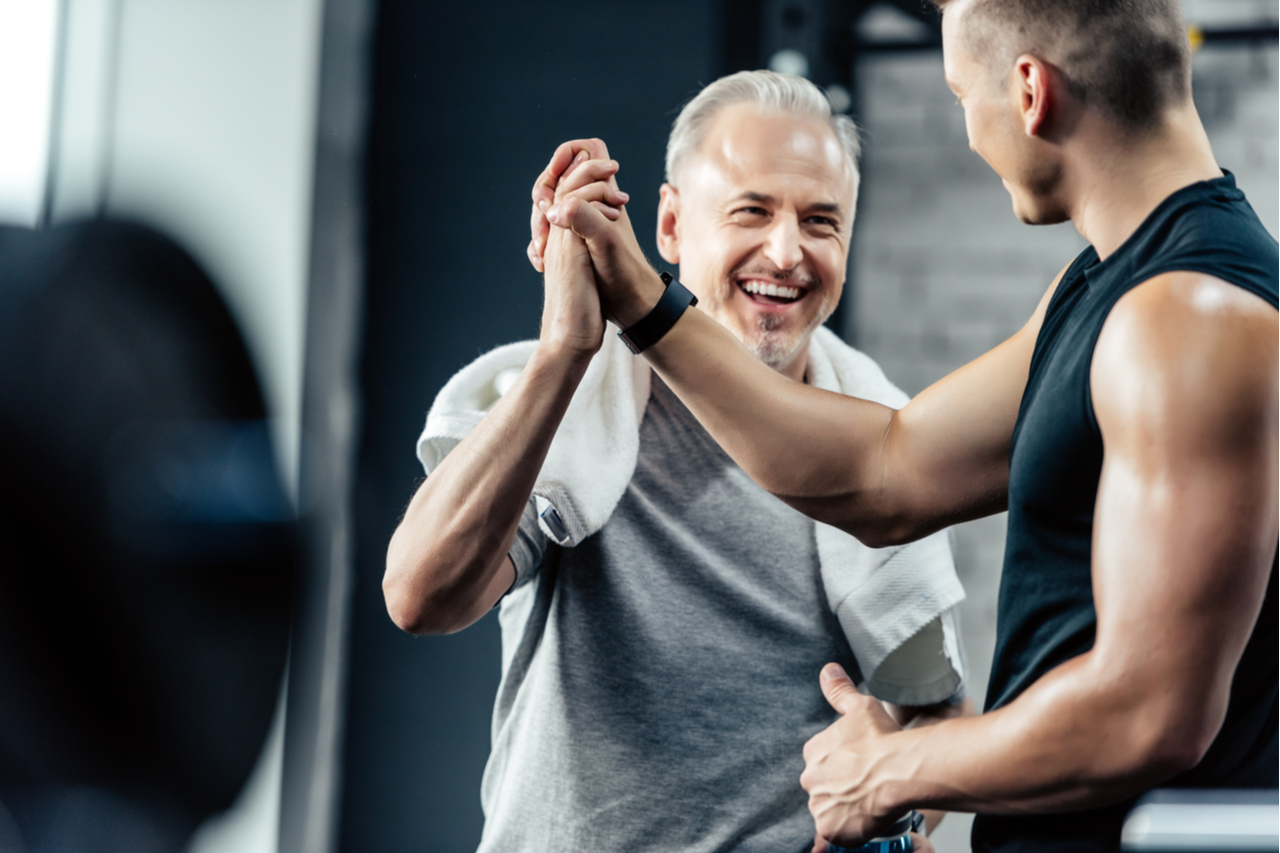 Senior sportsman giving highfive to trainer in sport center.