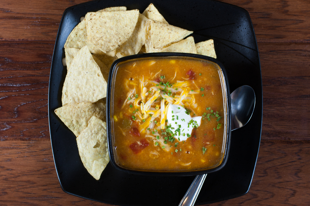 A bowl of chicken enchilada soup with a some tortilla on the side. 