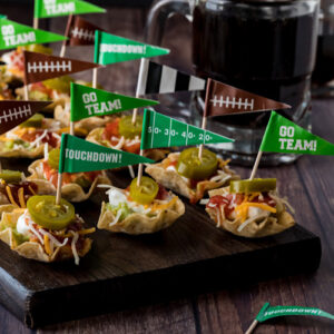 A close up view of a wooden platter of layered dip appetizers topped with jalapenos ready for a Super Bowl party.