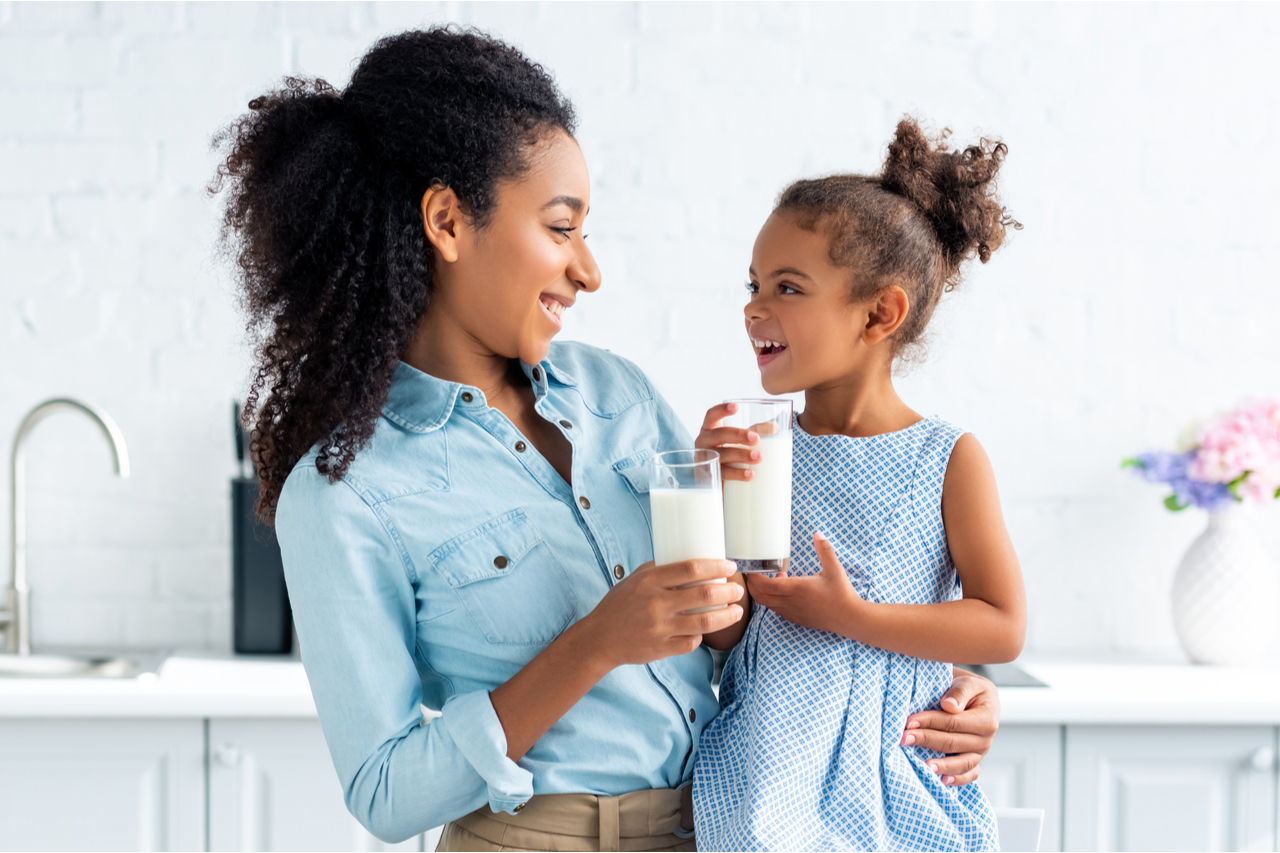 Mother and daughter holding glasses of milk in kitchen and looking at each other.