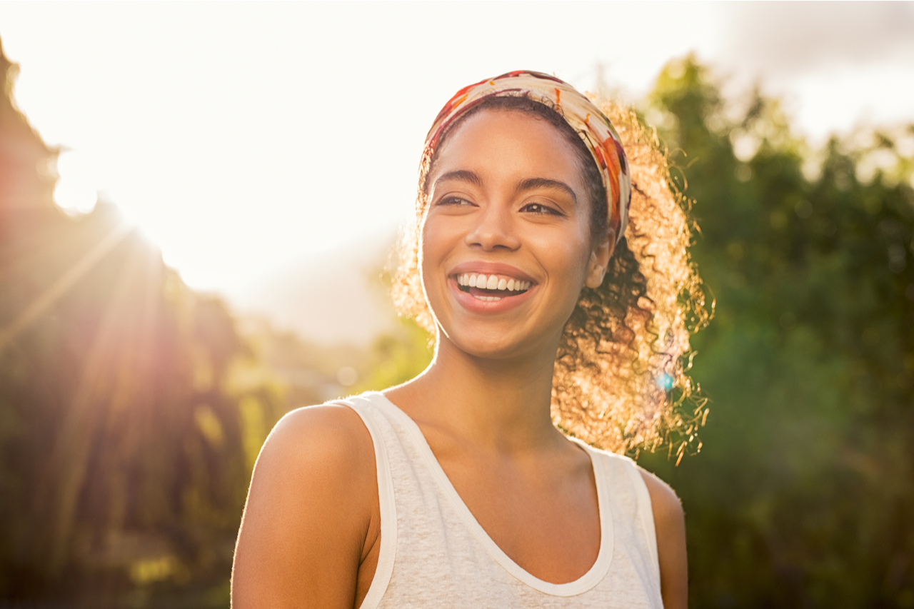 woman smiling and looking away at park during sunset figured how to manage stress.