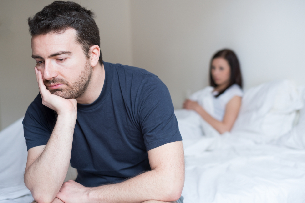 sad looking man sitting on the edge of the bed looking disappointed.