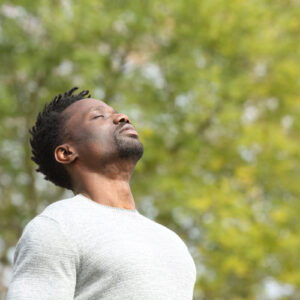 Black serious man breathing deeply fresh air in a park a sunny day with a green tree in the background