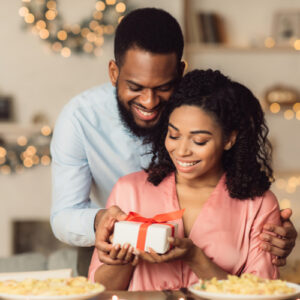 Guy presenting wrapped gift box to his excited girlfriend at cafe.