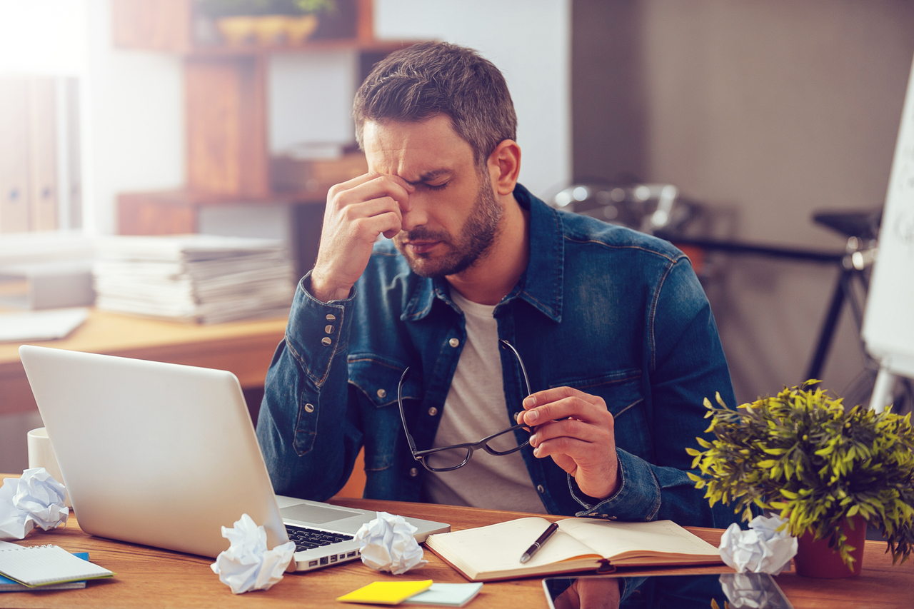 Frustrated young man massaging his nose and keeping eyes closed for stress awareness month.