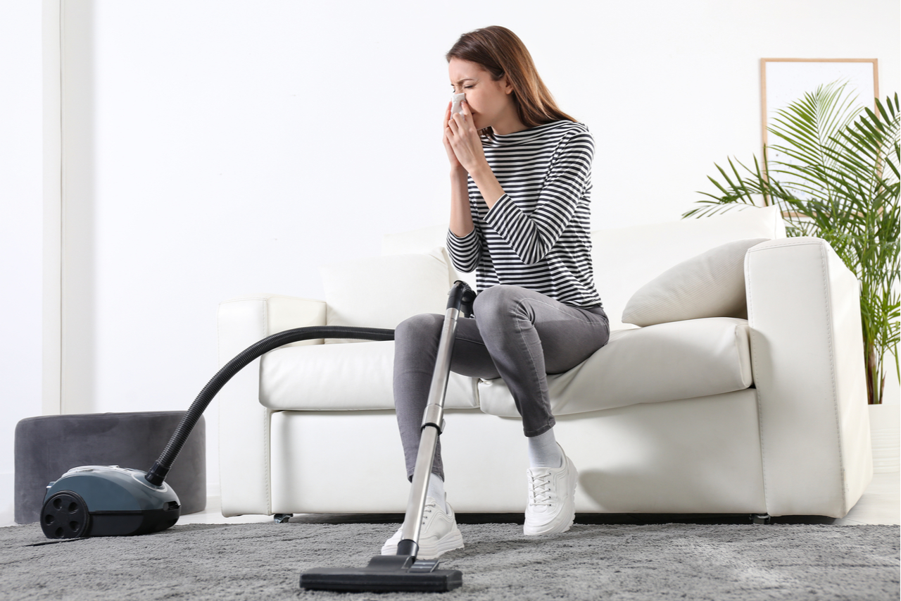 Woman suffering from dust allergy while vacuuming house that needs a healthy mind and body.