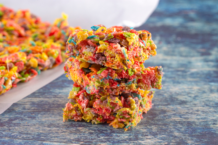 Fruity pebbles protein cheesecake frosting cereal treat bars on blue table.