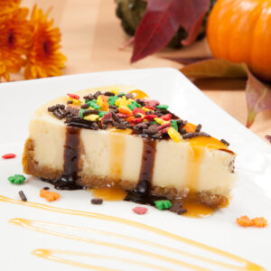 Sprinkle covered cheesecake with caramel and chocolate syrup with pumpkins and flowers in fall theme.