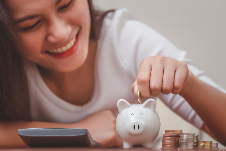 Woman hand putting money into piggy bank for saving money.