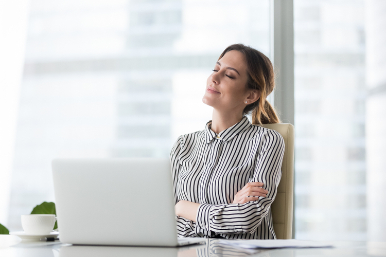 Smiling businesswoman sitting in office chair relaxing with eyes closed.