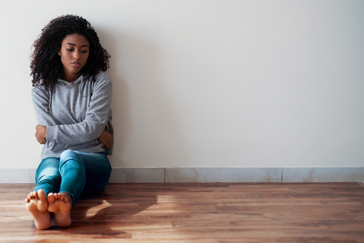 A woman sitting on the floor while hugging herself. 