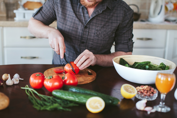 man's hands cut tomato on the board for a vegetarian salad