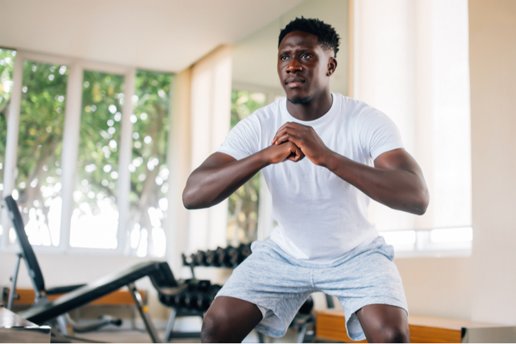 Man in sportswear warming up and doing squat exercise during workout.