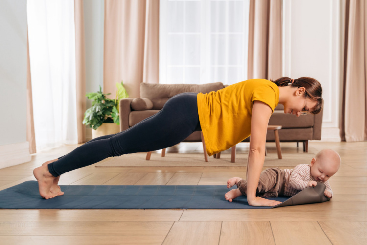 mom smiling at her baby while doing push up on exercising mat at home