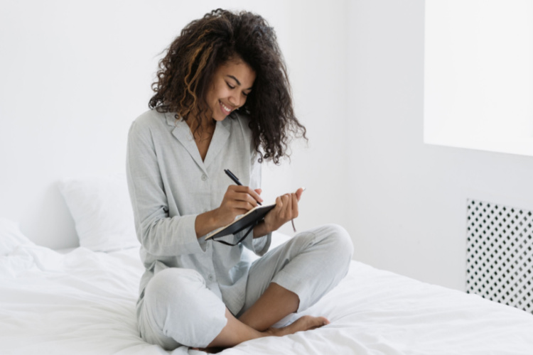 woman sitting on bed in writing in personal journal