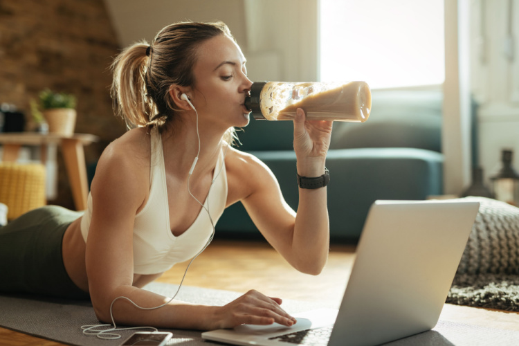 drinking protein shake while using laptop at home.