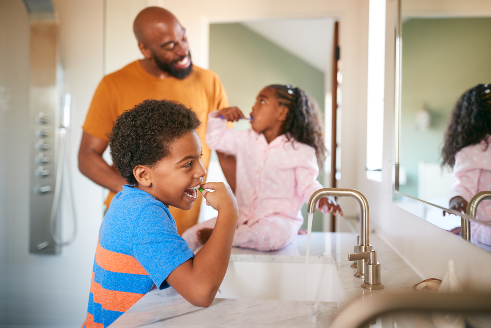 Father helping children to brush teeth in bathroom at home - childrens dental health