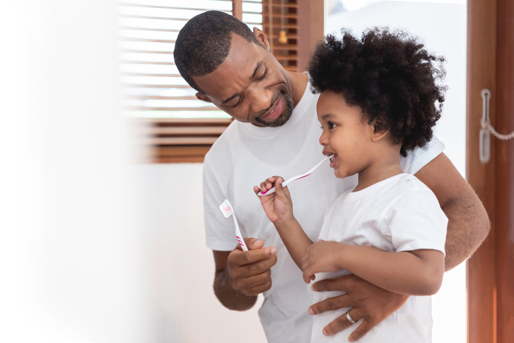 dad teaching his son in white shirt brushing teeth bathroom together to emphasize the importance of childrens dental health